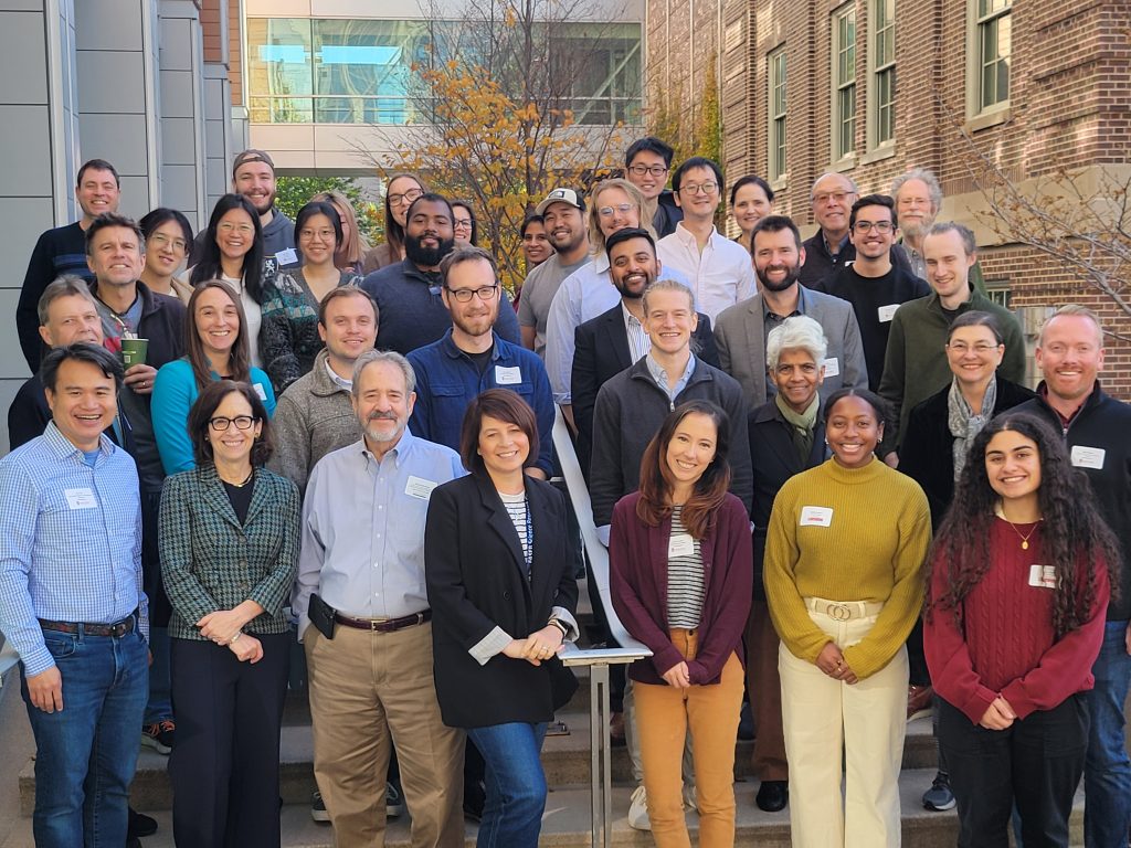 Group photo of faculty, staff, and students standing outside on a stairway smiling at the camera.