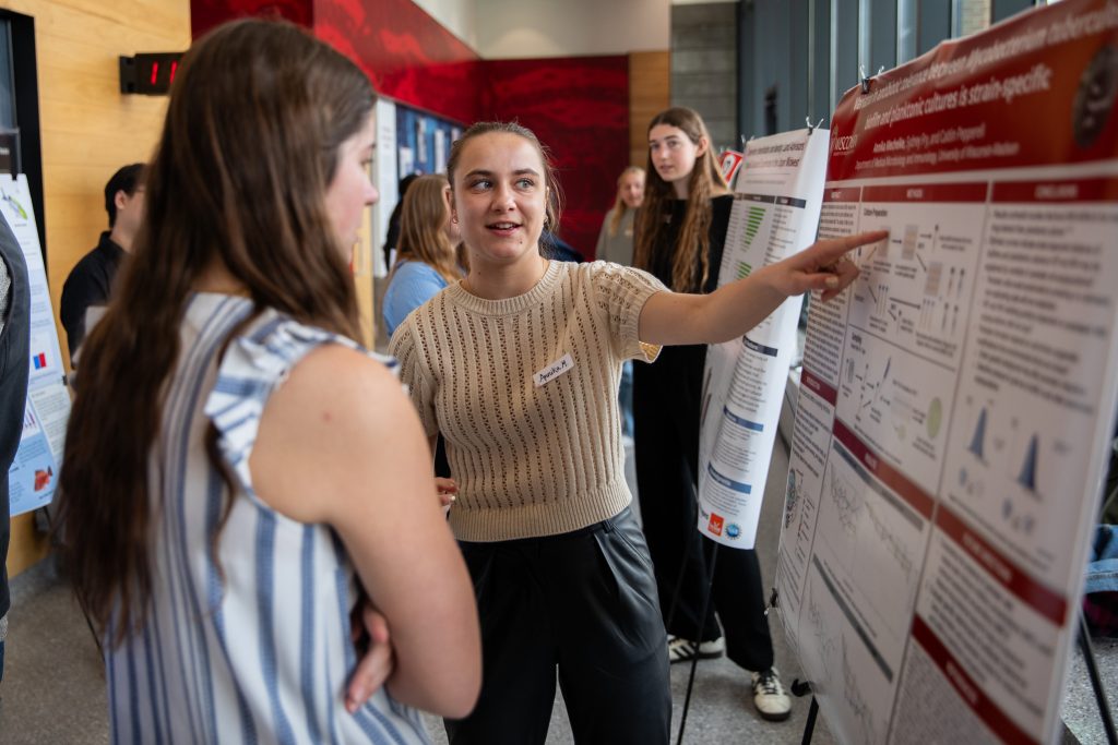 Young woman presents her research poster to another young woman
