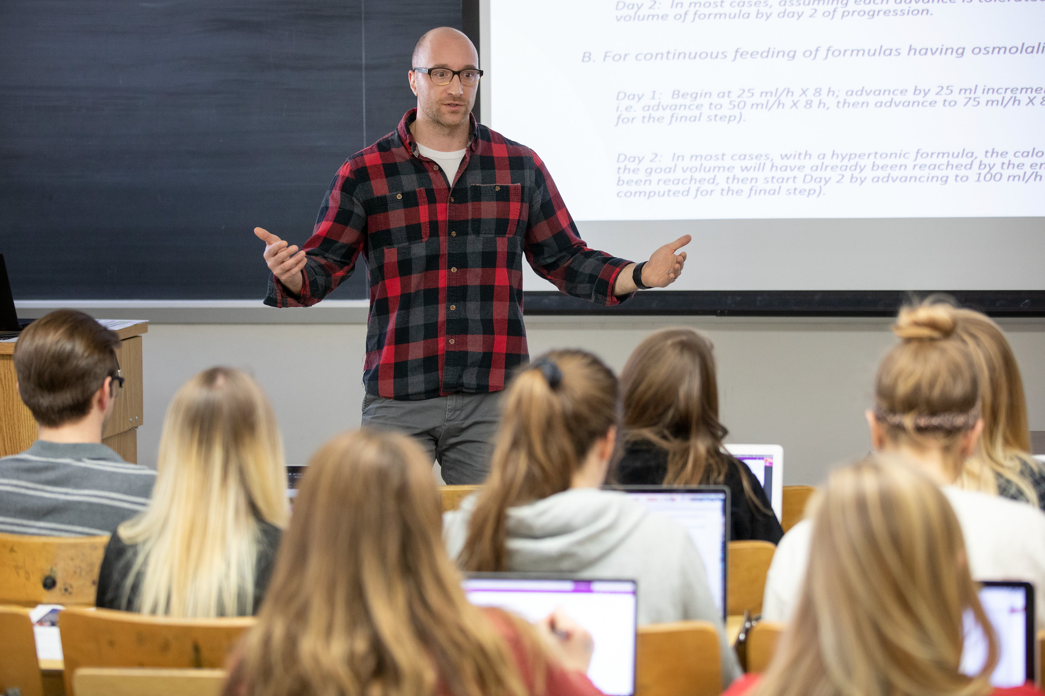 A person is standing at the front of a classroom talking to students
