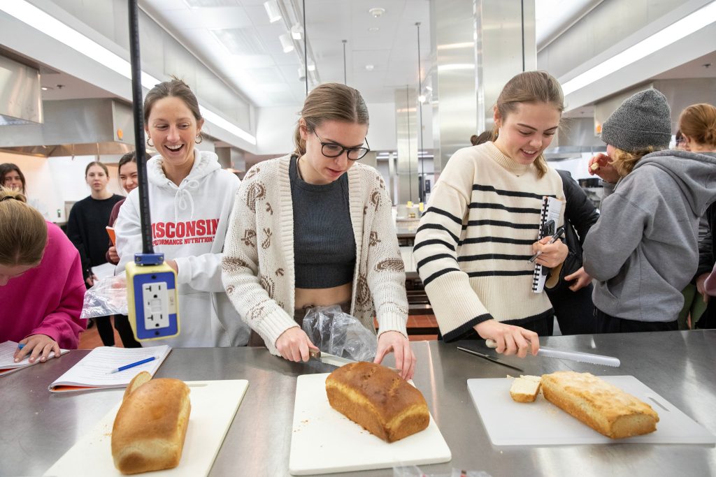 Three students cut loaves of bread