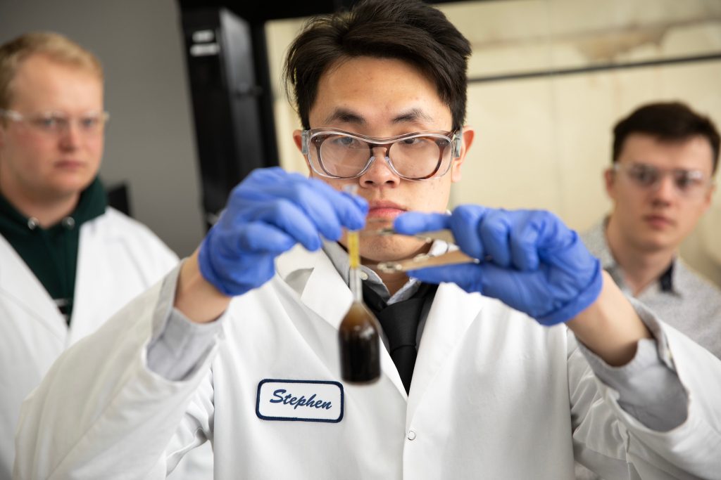 A student wearing a lab coat and goggles is conducting a test in a lab