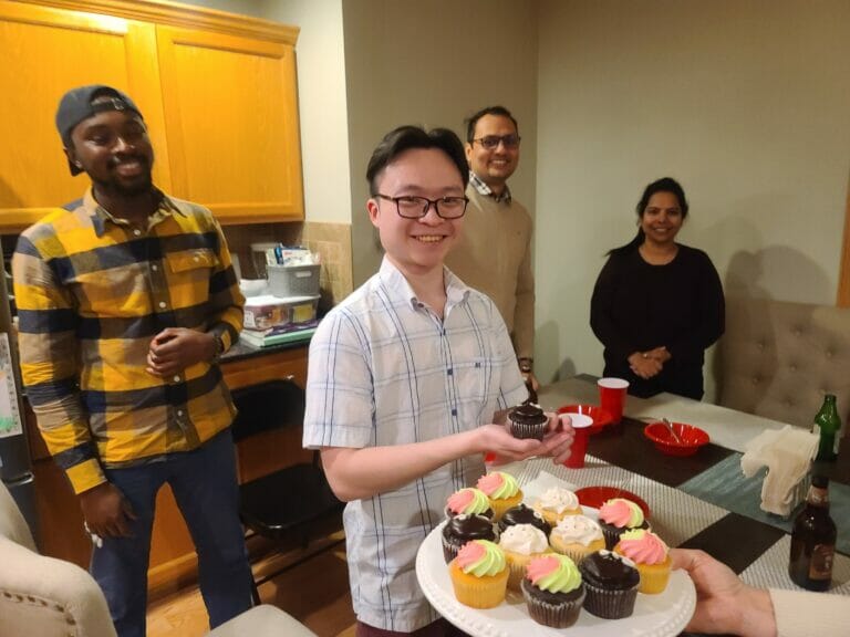Man standing smiling while holding a cupcake.
