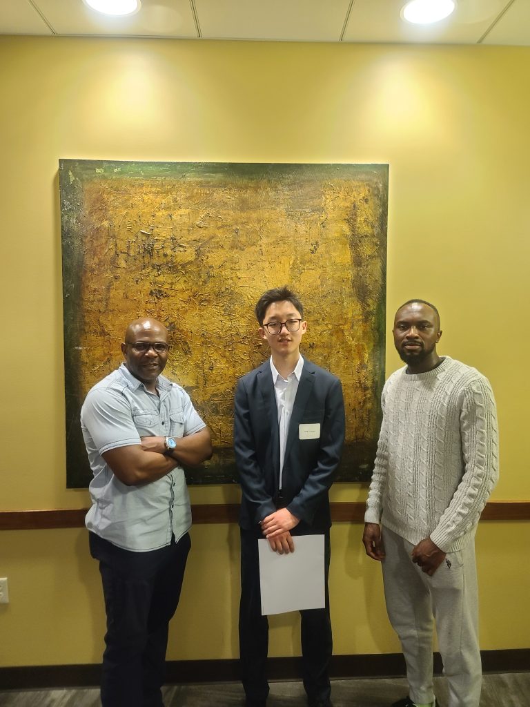 Left to right: Victor Ujor, Steven Hsieh, Eric Agyeman-Duah. They are standing in front of a yellow wall smiling at the camera, celebrating Steven who received the Hilldale Scholarship Award in2025.