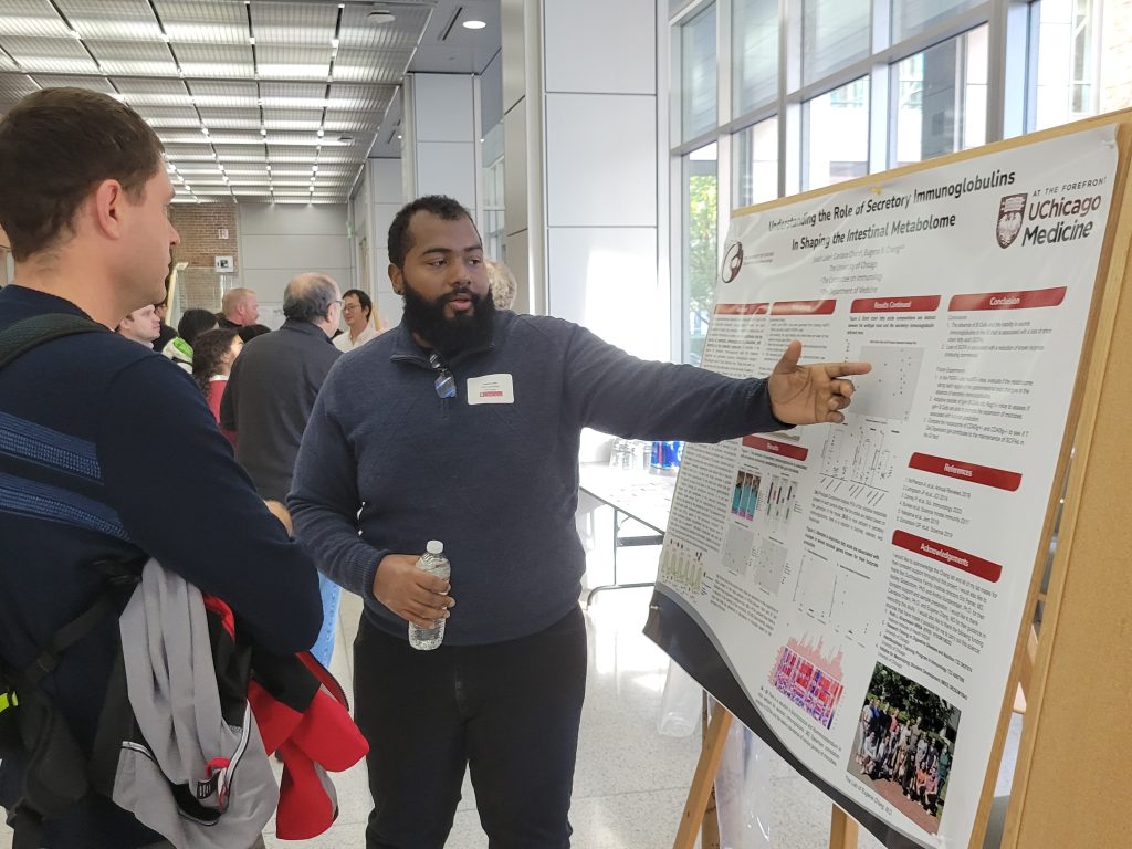 Man presenting his scientific poster to a small group of people at the 2024 MANTP Joint Retreat.