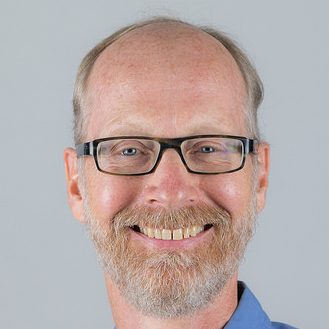 Man wearing blue shirt with glasses and a beard.